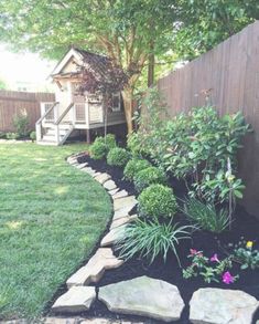 a garden with rocks and flowers in the grass near a fenced in backyard area