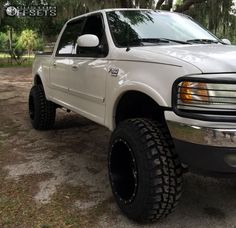 a white pickup truck parked on top of a dirt road in front of some trees