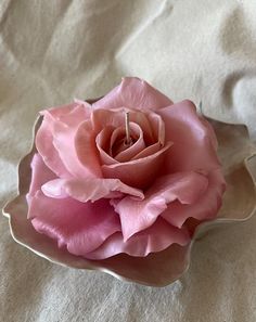 a single pink rose sitting on top of a white cloth covered tablecloth in the shape of a bowl