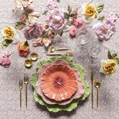 the table is set with pink flowers and gold cutlery, silverware, and napkins