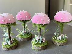 three pink mushrooms are sitting on top of moss covered trees and plants in small pots