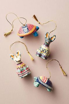 three ornaments are hanging from strings on a pink surface, one is wearing a hat and the other has an ornament in the shape of a turtle