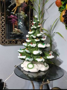 a glass table topped with a small christmas tree next to a painting on the wall