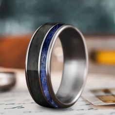 two wedding bands with blue and black inlays on each side, sitting on top of a piece of paper