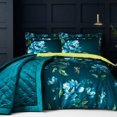 a bed with blue and green comforters in a dark room next to a lamp