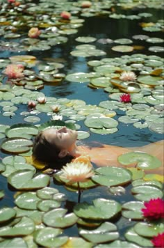 a woman floating on top of a body of water surrounded by lily pads and flowers