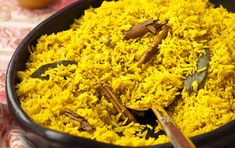 a bowl filled with rice and spices on top of a table cloth next to utensils