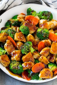 a white bowl filled with chicken, broccoli and carrots covered in sauce