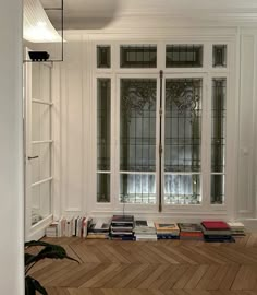 a room with some books on the floor and two windows in front of it,