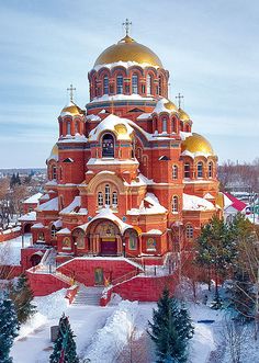 the church is surrounded by snow covered trees and evergreens, with gold domes on top