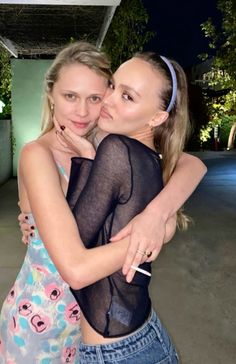 two young women hugging each other in front of an outdoor area with trees and buildings