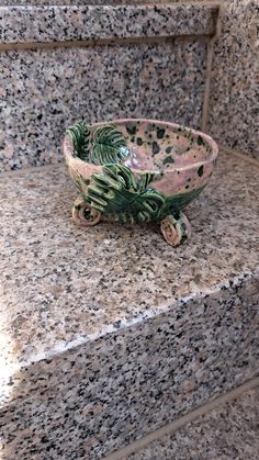 a bowl sitting on top of a granite step next to a planter filled with leaves