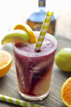 a purple drink with orange slices and a green striped straw in front of some lemons