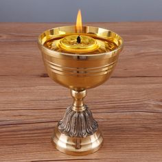 a gold colored chalice with a candle in the center on a wooden table top