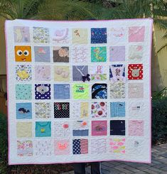 a woman holding up a large quilt made with squares and other fabric items in front of a palm tree