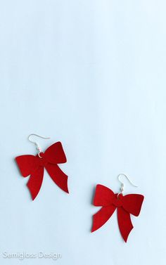 two red bows are hanging from earrings on a white surface, one is made out of felt and the other has silver earwires