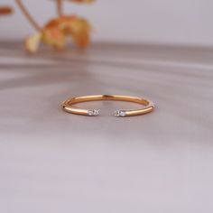 a gold ring with two small diamonds on the top and bottom, sitting next to a flower