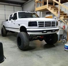 a white truck parked in a garage next to a stair case and some tires on the ground