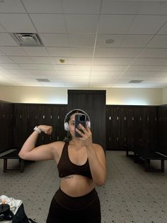 a woman wearing headphones taking a selfie in the locker room with her cell phone