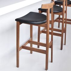 three wooden barstools with black leather seats are lined up against a white wall