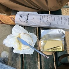 bread and butter are sitting on a picnic table next to a baguette knife