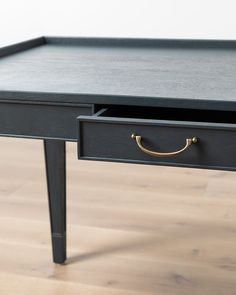 a black desk with gold handles on it's drawers and a wooden floor in the background