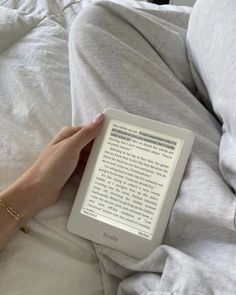 a person is laying in bed with their hand on an electronic device, reading the book