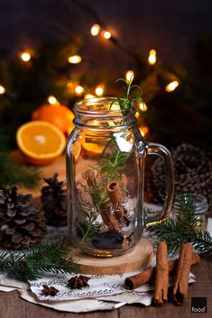 a glass jar filled with plants and oranges on top of a wooden table next to pine cones