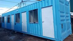 a blue and white container house sitting on top of a dirt ground next to a building