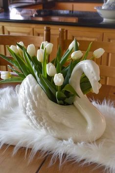 a white swan vase with tulips in it on top of a fur rug