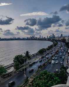 a city street filled with lots of traffic next to the ocean and tall buildings in the distance