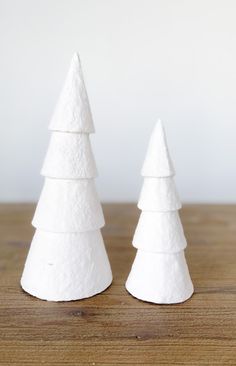 two small white christmas trees sitting on top of a wooden table