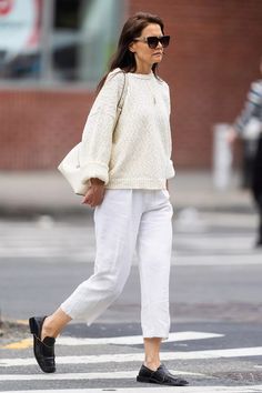 a woman walking across a street wearing white pants and a sweater with black trims