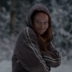 a woman in the snow wearing a hoodie and holding a tennis racquet