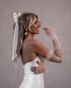 a woman in a white dress is smiling and holding her hands up to her face