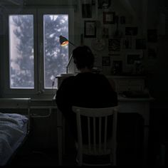 a person sitting at a desk in front of a window with a lamp on it