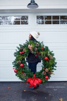 a woman holding a christmas wreath in front of a garage door