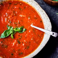 a bowl of tomato soup with basil leaves on the side and a spoon in it