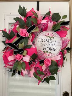 a wreath with pink flowers and green leaves hanging on the front door to say home sweet home