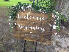 a welcome sign with flowers and greenery on it in front of a large tree