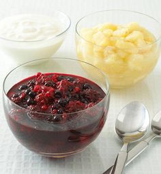 two bowls filled with fruit and yogurt next to spoons