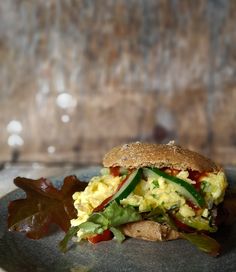 an egg salad sandwich with lettuce and tomato on a black plate against a wooden background