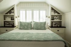 a bed sitting under a window in a bedroom next to a bookcase filled with books