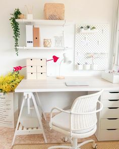 a white desk topped with a laptop computer next to a flower vase and shelf filled with books