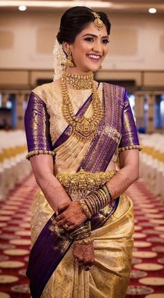 a woman wearing a gold and purple sari with jewelry on her neck, standing in front of rows of chairs