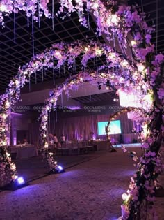 an archway decorated with purple flowers and fairy lights is lit up in the dark room