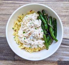 a white bowl filled with pasta, green beans and cream sauce on top of it