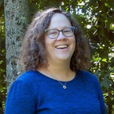 a woman wearing glasses standing in front of a tree smiling at the camera with her hands on her hips