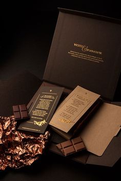 an assortment of chocolates and papers on a black surface with gold foil wrapping around them