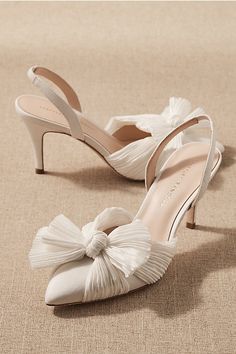 a pair of white shoes with a bow on the toe and heel, sitting on a beige surface